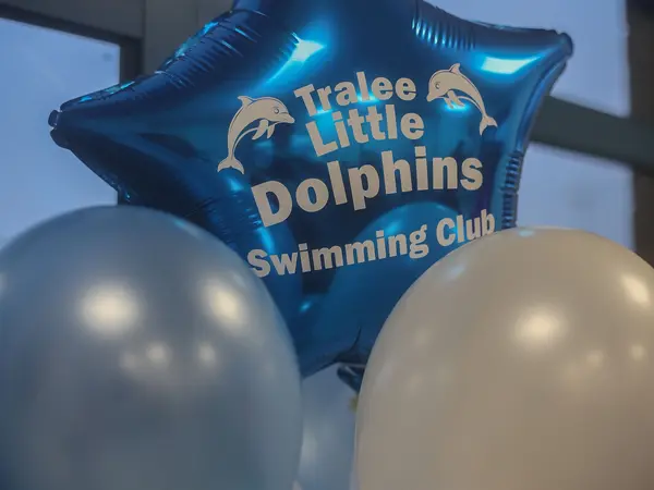 A blue star balloon printed with Tralee Little Dolphins Swimming Club among white and blue balloons