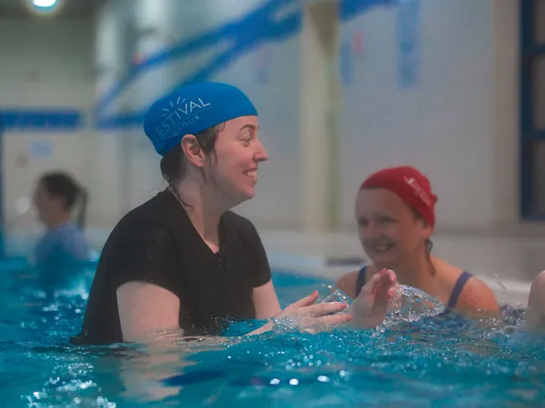 A coach chatting in the water with a parent and child in red swim caps