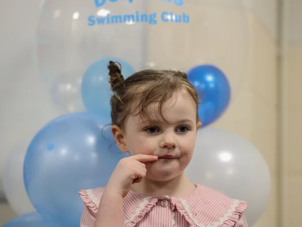 A young girl standing beside a column of club balloons at the party