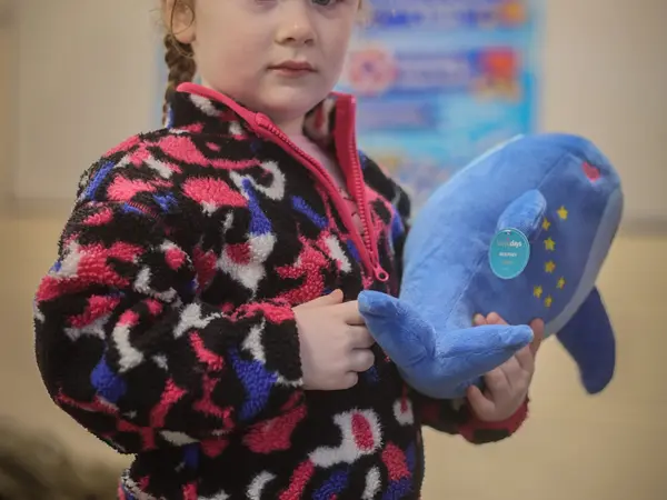 A girl hugging a blue dolphin plush toy at the Open Day party