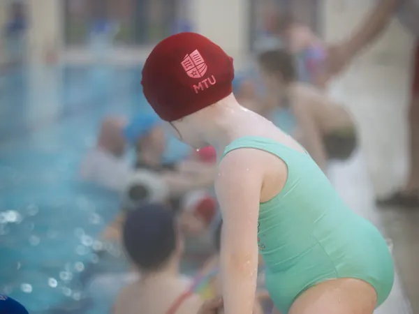 A young girl in a green swimsuit being helped into the pool