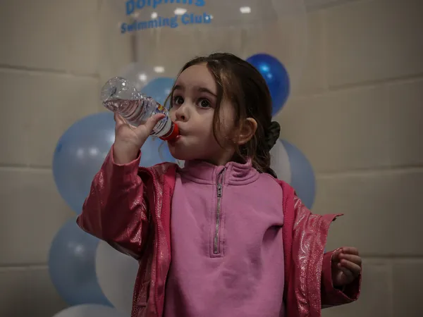 A girl in pink having a drink beside the party balloons