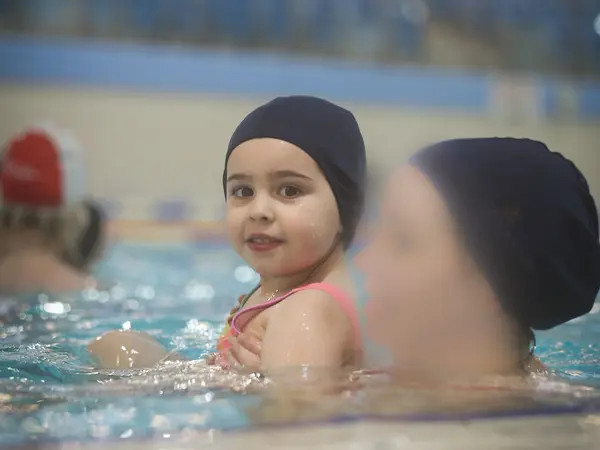 A young girl in a swim cap smiling at the edge of the pool