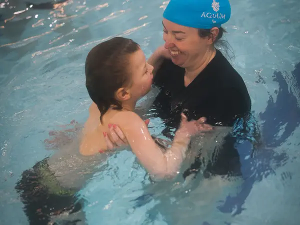 An instructor lifting a smiling child in the water