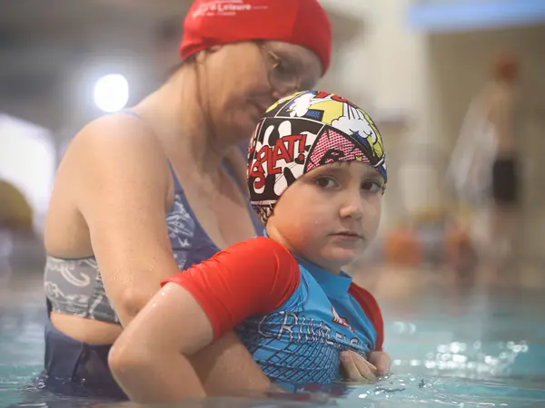 A mother supporting her son wearing armbands in the water