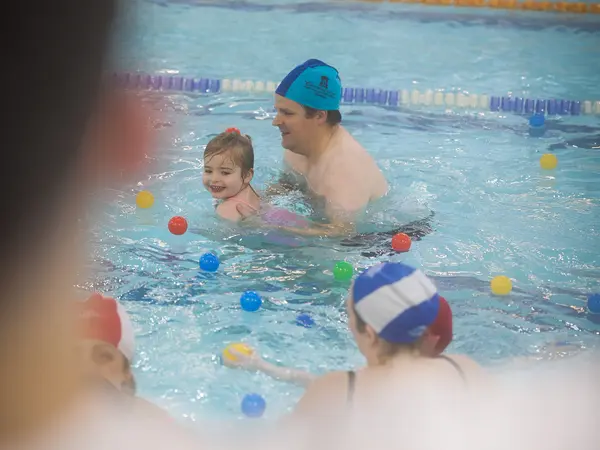 A toddler playing ball games in the pool with a parent