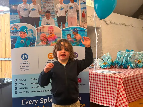 A boy waving in front of the Tralee Little Dolphins club banner