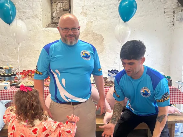 Two coaches in club jerseys chatting with a young girl at the farm party