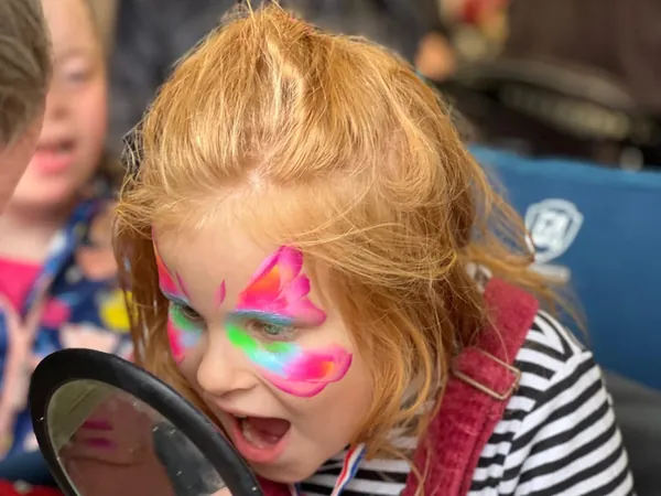 A girl checking her colourful butterfly face paint in a hand mirror