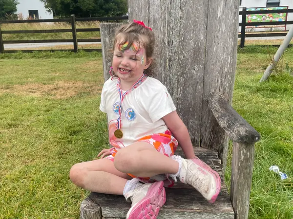 A girl with face paint sitting on a big wooden chair