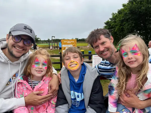 Children and adults with colourful face paint smiling together outdoors