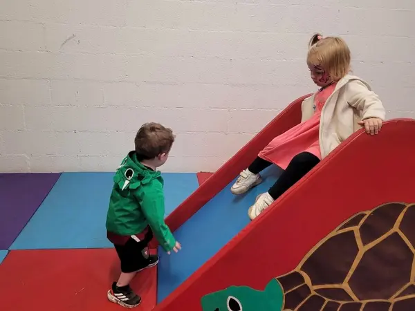 Two children playing on the slide in the indoor play area