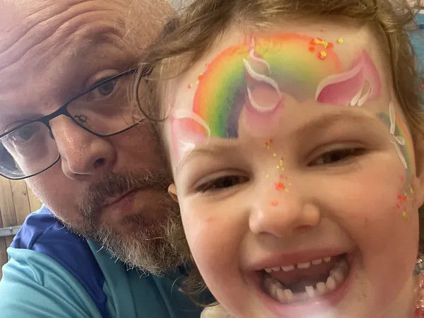 A girl with rainbow unicorn face paint grinning for a selfie