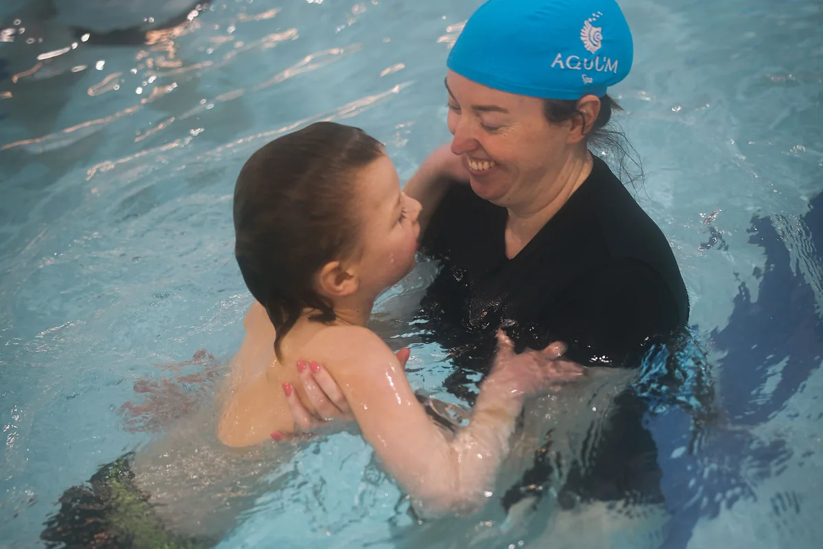 A coach lifting a smiling child in the pool during a lesson