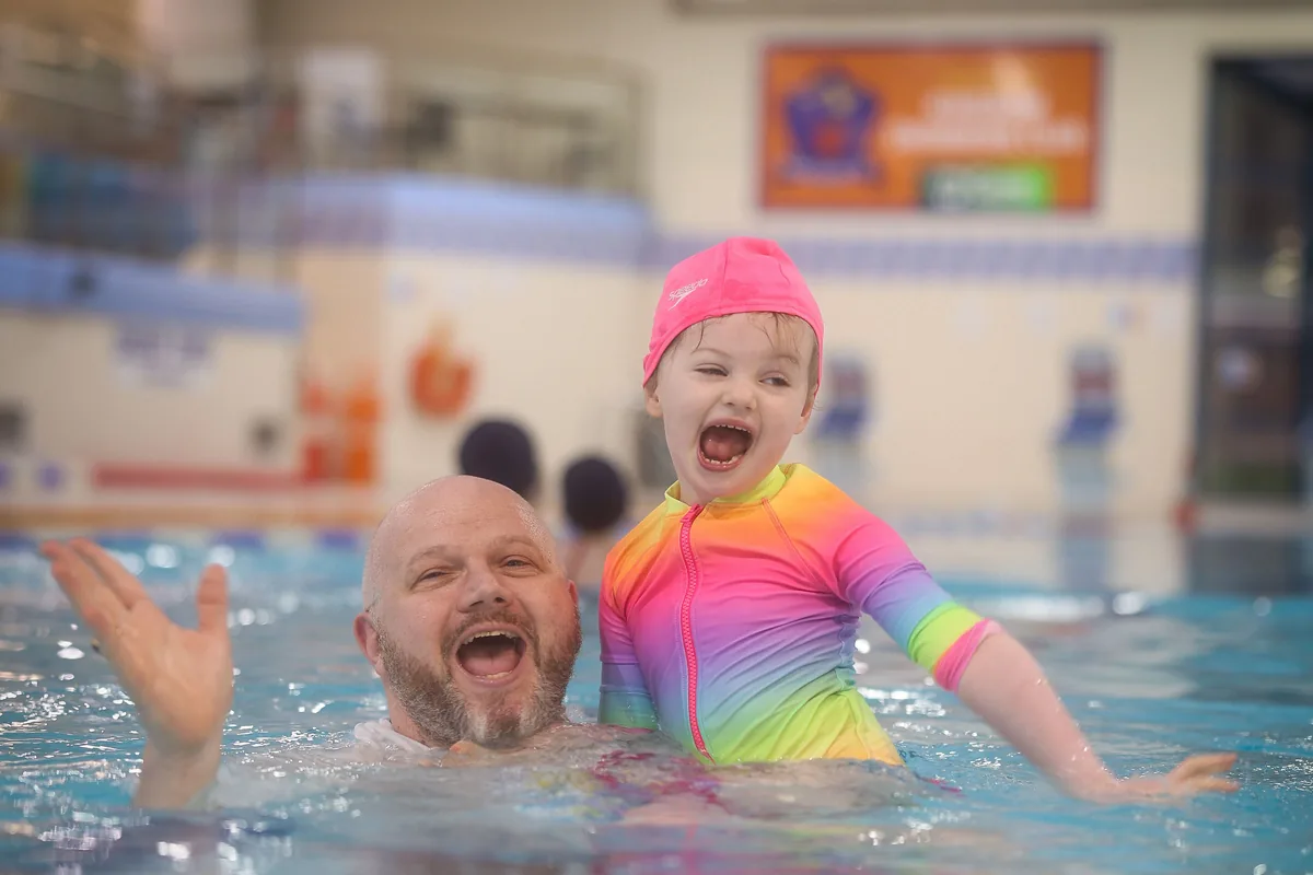 A father and his young daughter splashing and laughing together in the pool