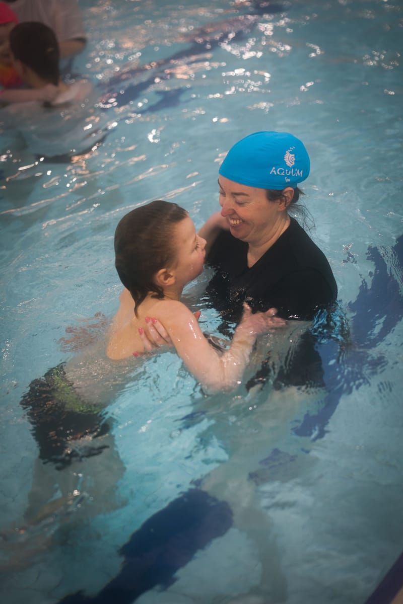 A coach supporting a smiling child in the water during a lesson