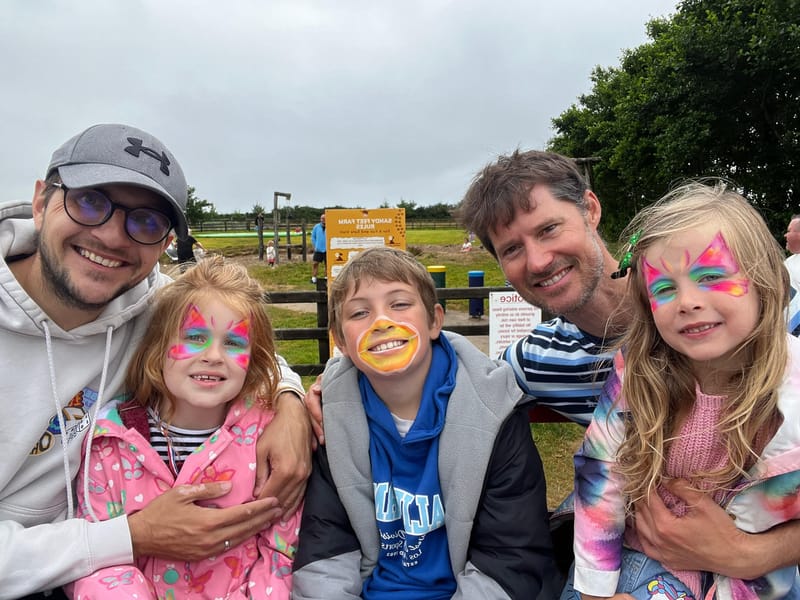 Children and adults with colourful face paint together at Sandy Feet Farm